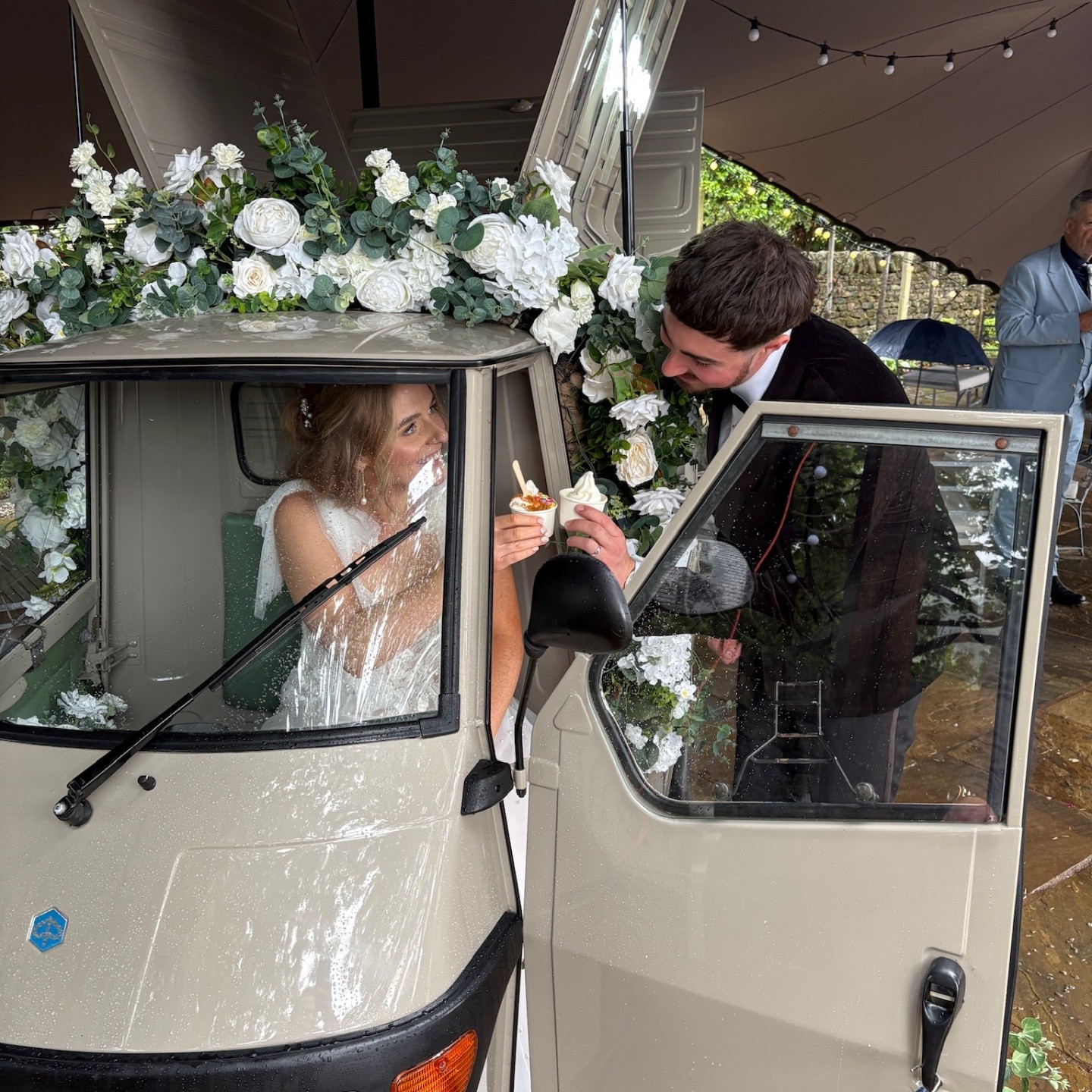 Bride and groom enjoying ice cream in the vintage floral tuk-tuk at a wedding